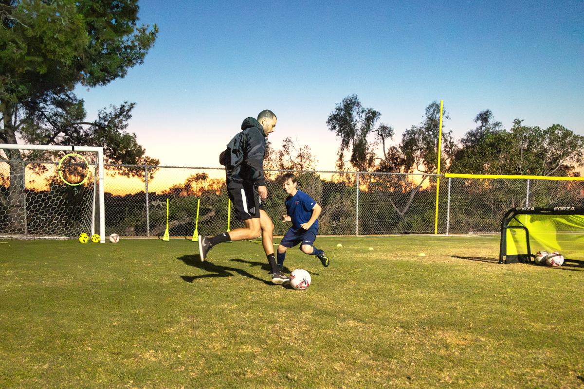 Coach Luka and a young player driving at the ball at sunset, The Soccer Lab, Carlsbad