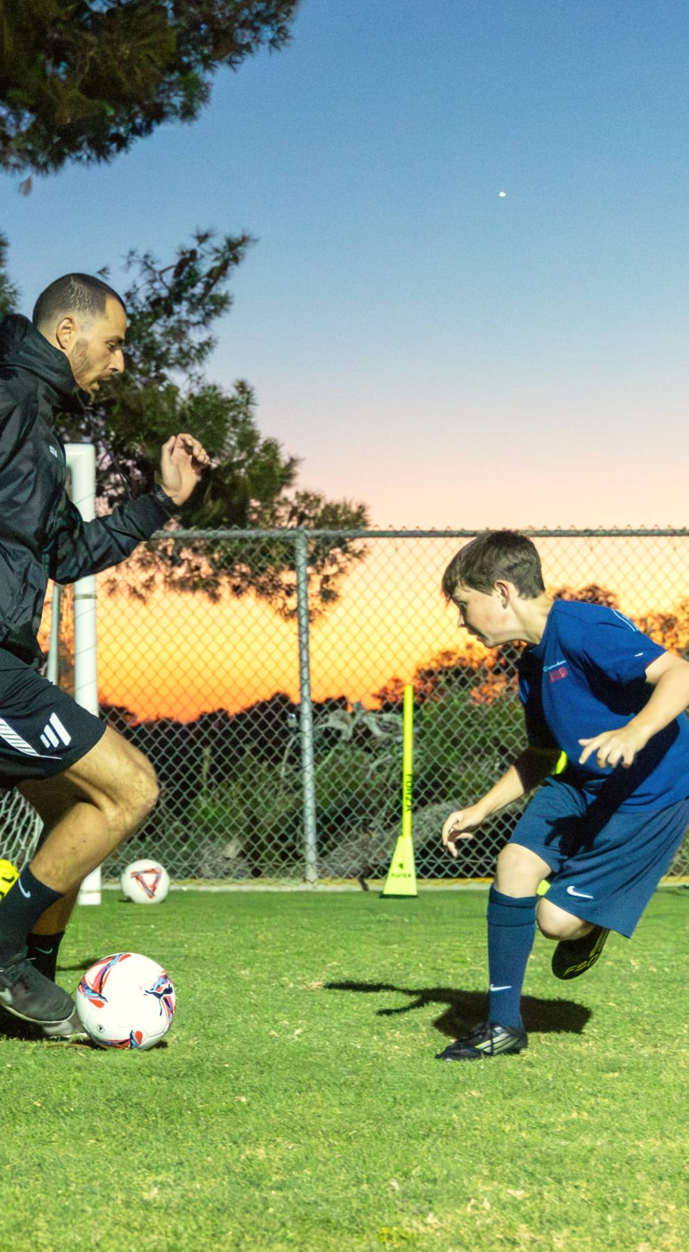 Coach Luka and a young player driving at the ball together at dusk, The Soccer Lab, Carlsbad